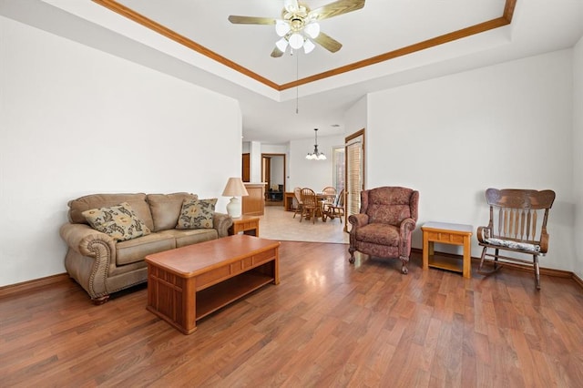 living room with ceiling fan with notable chandelier, wood finished floors, a raised ceiling, and baseboards