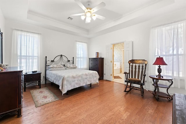 bedroom featuring multiple windows, a raised ceiling, visible vents, and light wood-style floors