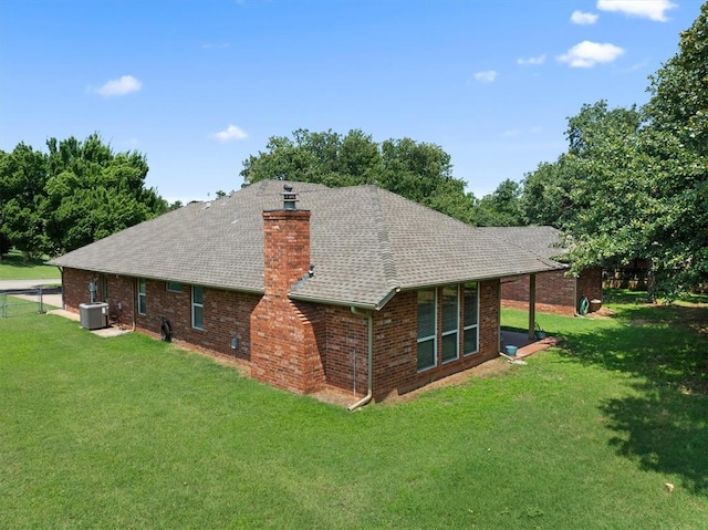 back of house with central air condition unit, brick siding, a chimney, and a yard