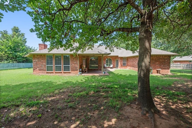 back of house featuring brick siding, fence, a yard, a chimney, and a patio area