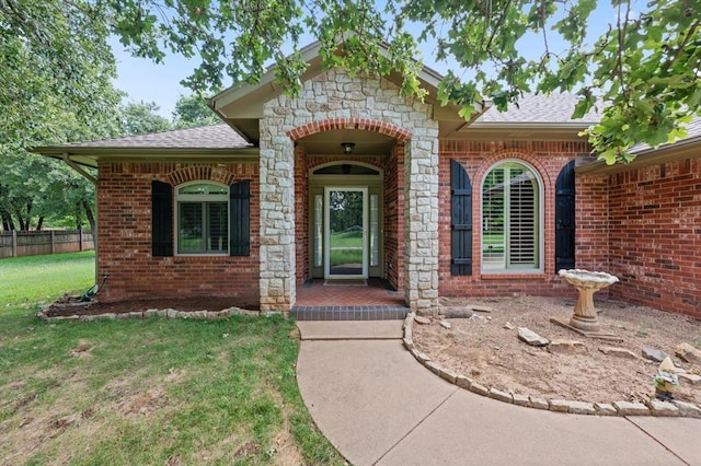 view of exterior entry with stone siding, brick siding, a lawn, and a shingled roof