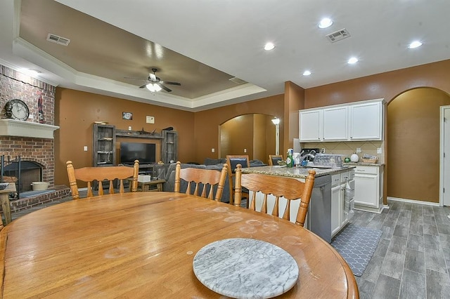 dining area with a brick fireplace, a tray ceiling, ceiling fan, sink, and hardwood / wood-style flooring