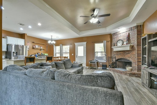 living room featuring a raised ceiling, a wealth of natural light, light hardwood / wood-style floors, and a brick fireplace