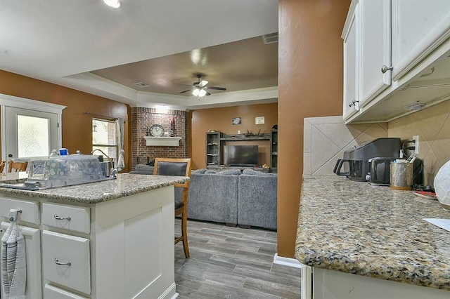 kitchen featuring white cabinetry, ceiling fan, light stone countertops, a brick fireplace, and light hardwood / wood-style flooring