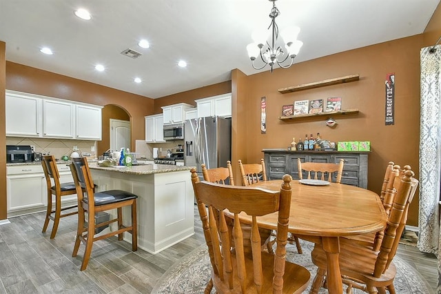 kitchen featuring pendant lighting, an inviting chandelier, white cabinets, an island with sink, and appliances with stainless steel finishes