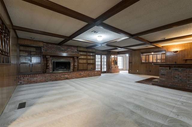 unfurnished living room featuring beamed ceiling, a textured ceiling, light colored carpet, and wood walls