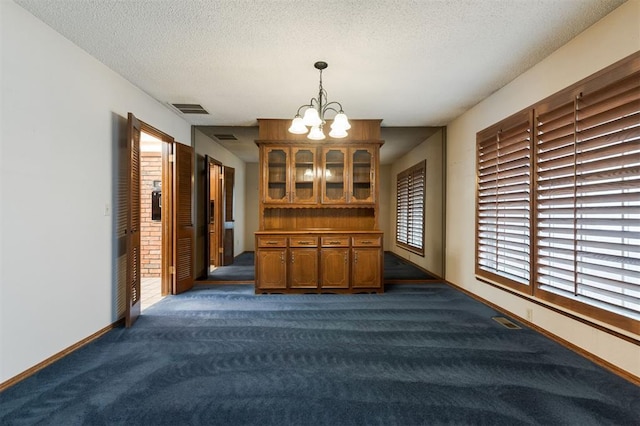 interior space featuring an inviting chandelier, a textured ceiling, and dark colored carpet