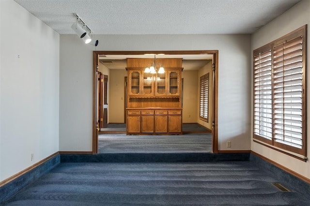 unfurnished room with a notable chandelier, rail lighting, a textured ceiling, and dark colored carpet