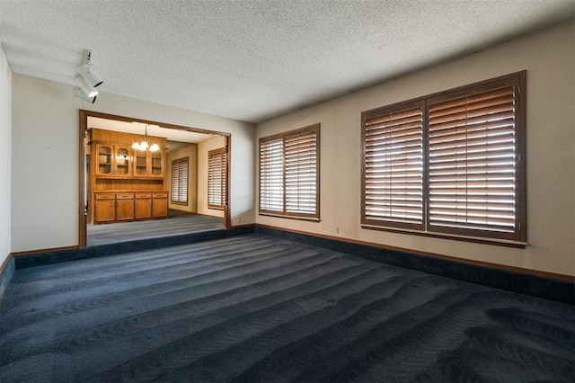 empty room featuring carpet flooring, a textured ceiling, and a notable chandelier