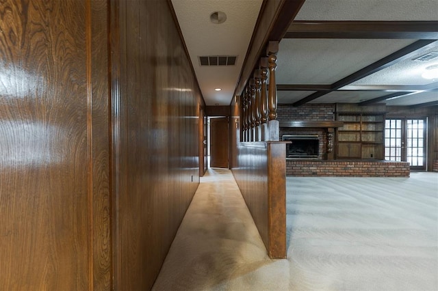 hall with light carpet, a textured ceiling, beamed ceiling, and wood walls