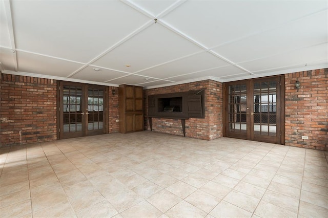 unfurnished living room with light tile patterned flooring, brick wall, and french doors