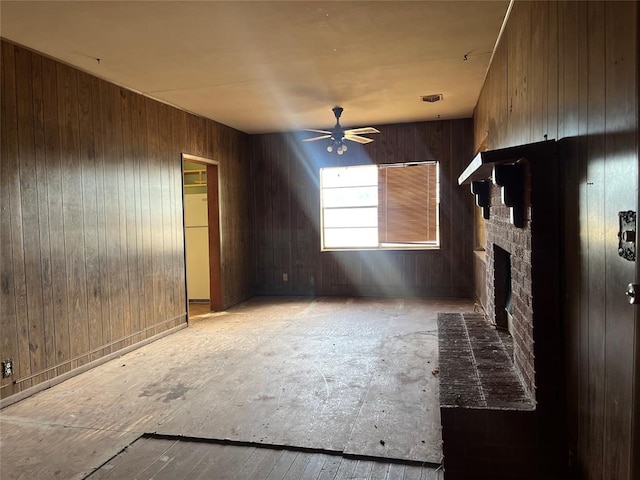 unfurnished living room with ceiling fan, a fireplace, and wood walls