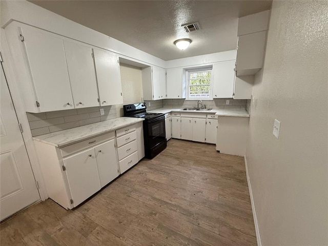 kitchen featuring light wood-type flooring, tasteful backsplash, black range with electric stovetop, sink, and white cabinetry