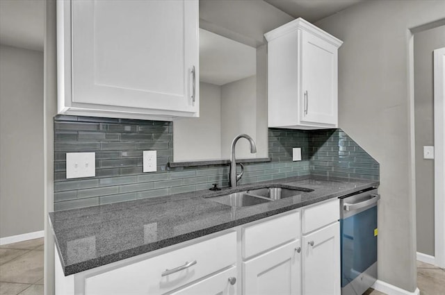 kitchen featuring dark stone counters, white cabinets, sink, stainless steel dishwasher, and decorative backsplash