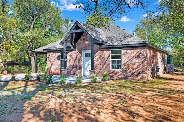 view of front of house with roof with shingles, central air condition unit, a patio, and brick siding