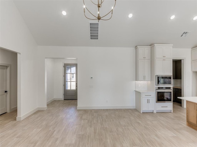 kitchen with light hardwood / wood-style flooring, white cabinets, stainless steel appliances, and decorative light fixtures