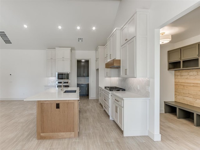 kitchen with white cabinets, backsplash, stainless steel appliances, and an island with sink