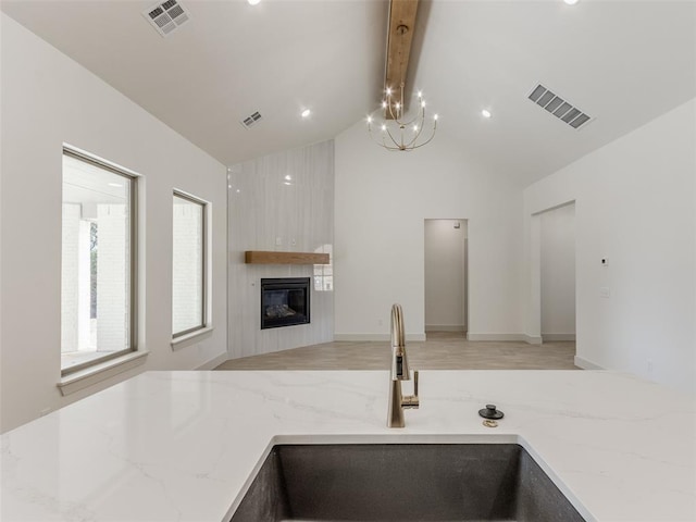 kitchen featuring lofted ceiling with beams, a large fireplace, light stone countertops, and sink