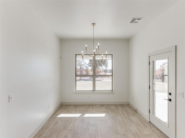 unfurnished dining area with light wood-type flooring, plenty of natural light, and a notable chandelier