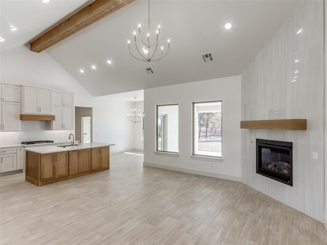 kitchen featuring beam ceiling, white cabinetry, a large fireplace, light hardwood / wood-style flooring, and a spacious island