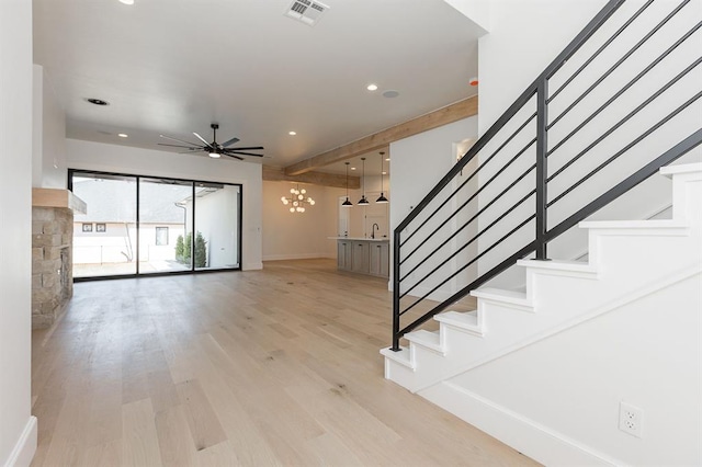 stairway featuring hardwood / wood-style flooring, ceiling fan with notable chandelier, a stone fireplace, and sink