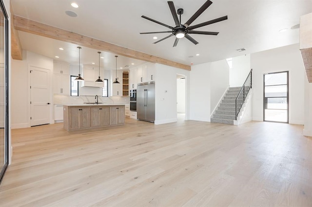 unfurnished living room with ceiling fan, sink, beamed ceiling, and light wood-type flooring