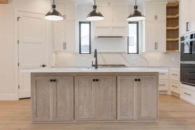 kitchen with light wood-type flooring, decorative light fixtures, a kitchen island with sink, and sink