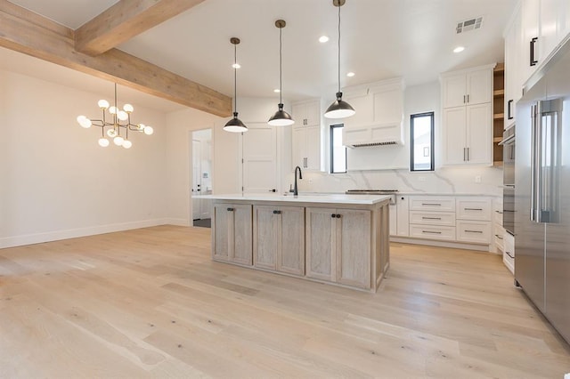 kitchen with light wood-type flooring, pendant lighting, a center island with sink, beamed ceiling, and white cabinetry