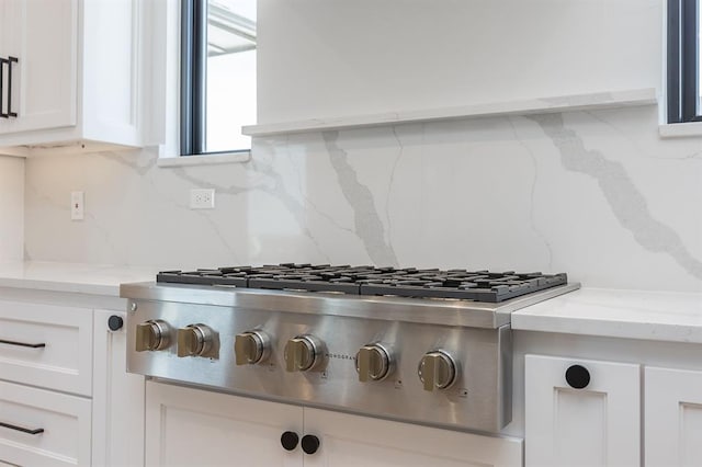 details with tasteful backsplash, white cabinetry, light stone counters, and stainless steel gas stovetop