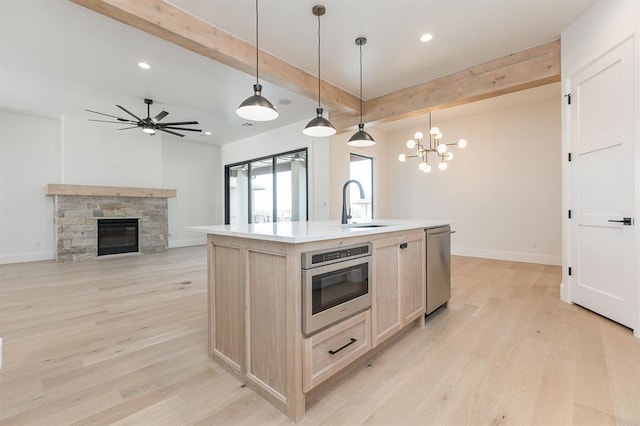 kitchen featuring pendant lighting, a kitchen island with sink, light wood-type flooring, a fireplace, and stainless steel appliances