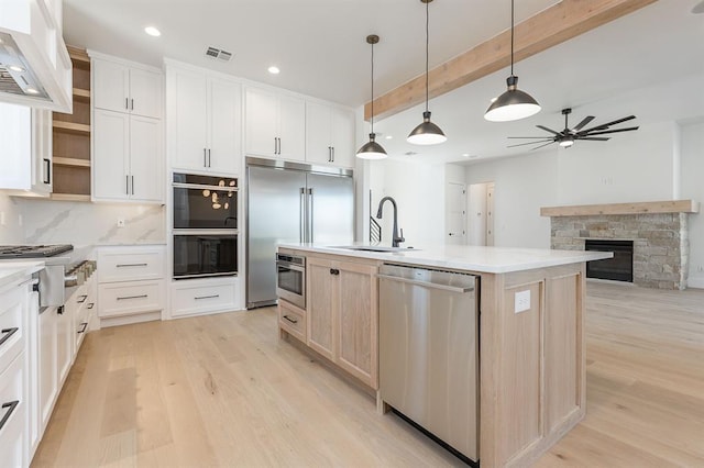 kitchen featuring white cabinetry, a stone fireplace, light hardwood / wood-style flooring, a center island with sink, and appliances with stainless steel finishes