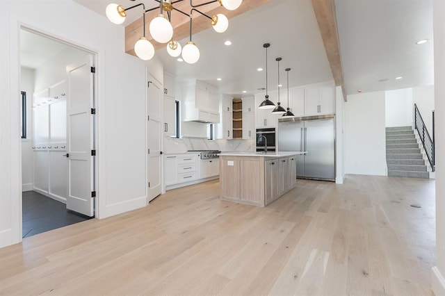 kitchen featuring decorative light fixtures, white cabinetry, stainless steel appliances, and an island with sink