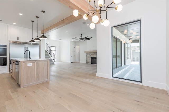 kitchen with beamed ceiling, an island with sink, light hardwood / wood-style floors, decorative light fixtures, and stainless steel built in fridge