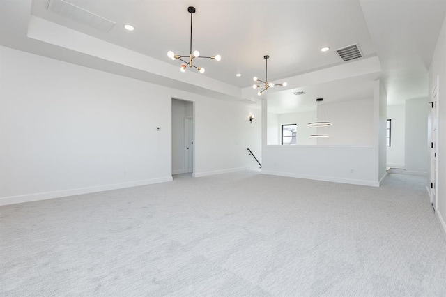 unfurnished living room with a chandelier, light colored carpet, and a tray ceiling