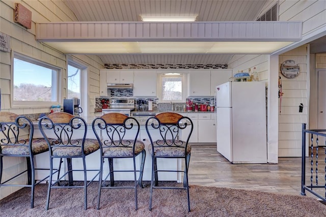 kitchen with white cabinets, plenty of natural light, white fridge, and light hardwood / wood-style floors