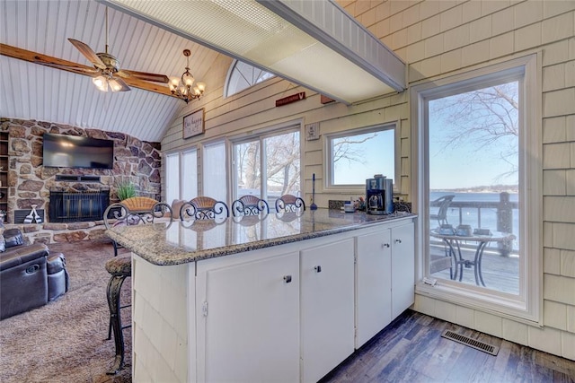 kitchen featuring light stone counters, dark hardwood / wood-style flooring, vaulted ceiling, a breakfast bar, and white cabinets