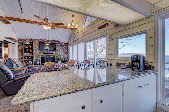 kitchen with ceiling fan with notable chandelier, vaulted ceiling with beams, white cabinetry, and light stone counters