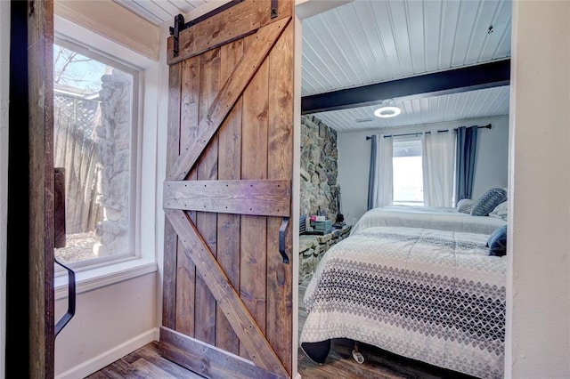 bedroom with a barn door, hardwood / wood-style floors, beamed ceiling, and wooden ceiling