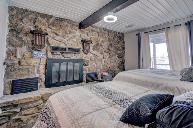 bedroom with beam ceiling and a stone fireplace