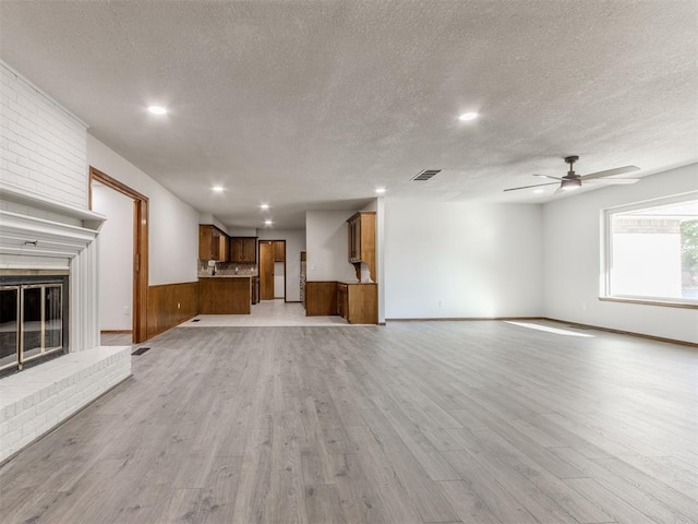 unfurnished living room featuring a textured ceiling, light wood-type flooring, a brick fireplace, and ceiling fan