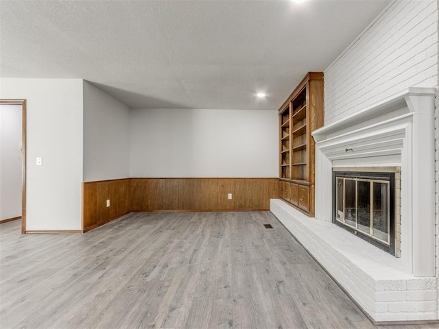 unfurnished living room featuring wood walls, built in features, light wood-type flooring, and a brick fireplace