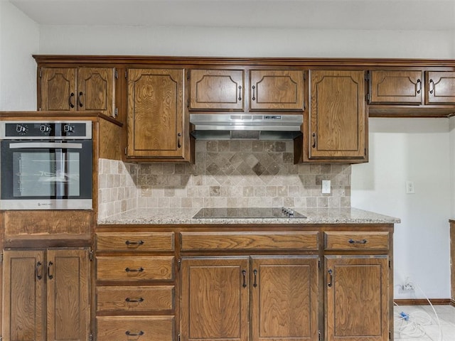 kitchen featuring backsplash, black electric cooktop, oven, and light stone counters