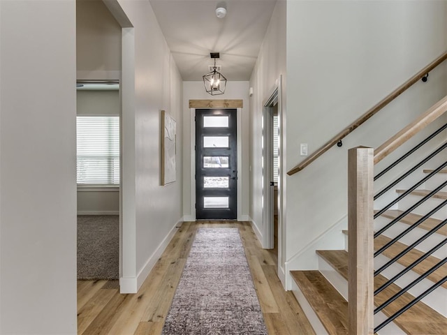 foyer entrance featuring a chandelier, stairway, baseboards, and wood finished floors