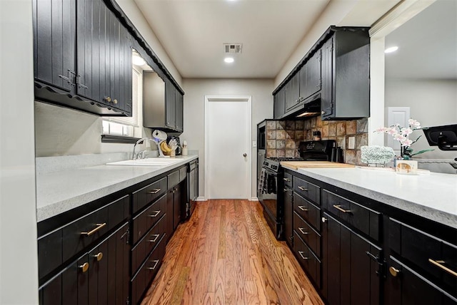 kitchen featuring black gas range, decorative backsplash, light wood-type flooring, and sink