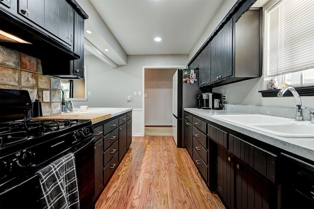 kitchen featuring stainless steel fridge, black gas stove, sink, and light hardwood / wood-style flooring