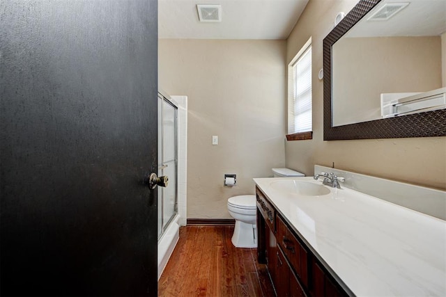 bathroom with hardwood / wood-style floors, vanity, toilet, and a shower with door