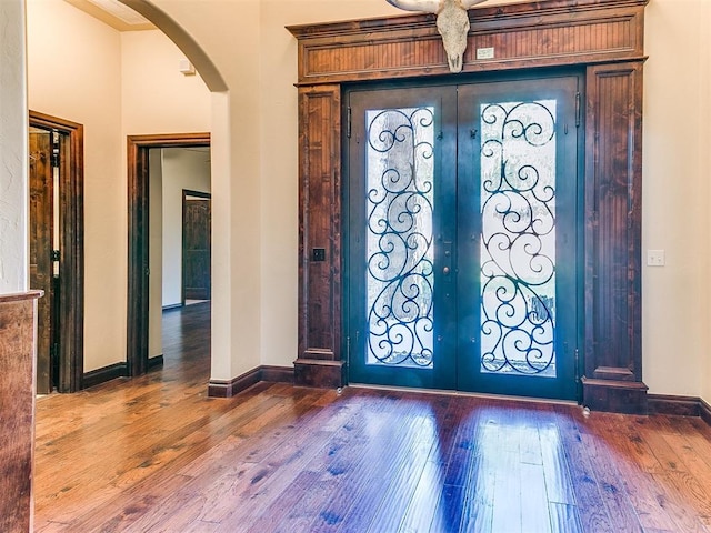 entrance foyer featuring hardwood / wood-style flooring, baseboards, arched walkways, and french doors