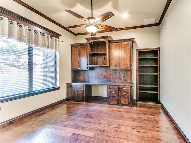 unfurnished office with dark hardwood / wood-style floors, ceiling fan, built in desk, and crown molding