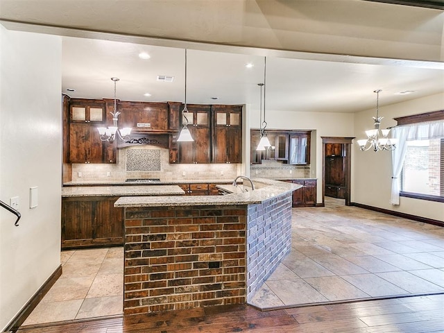 kitchen featuring dark brown cabinetry, an inviting chandelier, tasteful backsplash, and stainless steel gas stovetop