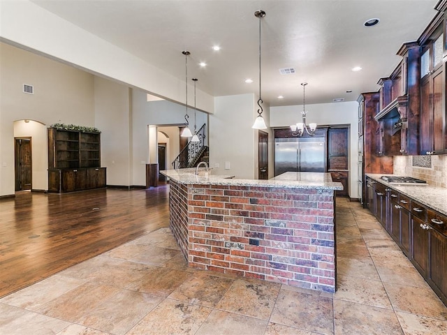 kitchen featuring light stone counters, arched walkways, stainless steel appliances, backsplash, and a large island with sink